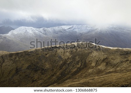 A background photo of Scottish Highlands in early winter. Beautiful snowy hilltops of otherwise green mountains.