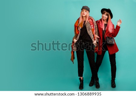 Couple of models pointing with surprised  faces on  turquoise background in studio.in stylish leopard print faux fur coat and wool scarf posing on turquoise background. Full length. 