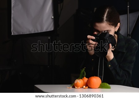 Young woman taking picture of fresh tangerines in professional studio