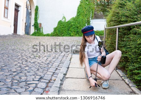 A girl with long hair sets a tripod with a telephone on the street.