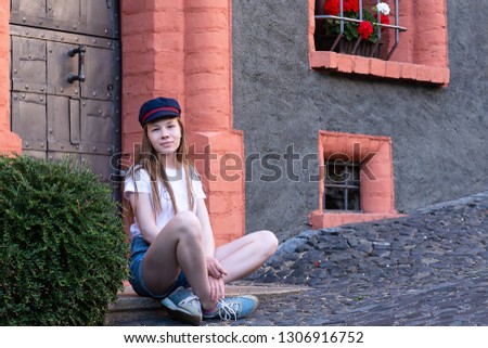 A girl sits near a beautiful home and smiles sweetly.