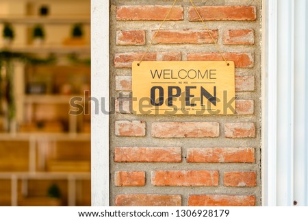 Business open and welcome wooden sign board at bricks wall beside the door.