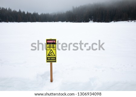 Frozen lake covered in winter snow, with a "Danger. Lake Not Monitored. Ski Area Boundary" sign