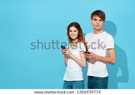 cute young cute young couple in white T-shirts with phones in their hands communicate with each other on a blue isolated background