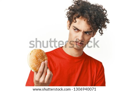 Curly guy in a red T-shirt with a hamburger in his hands against a gray background fast food