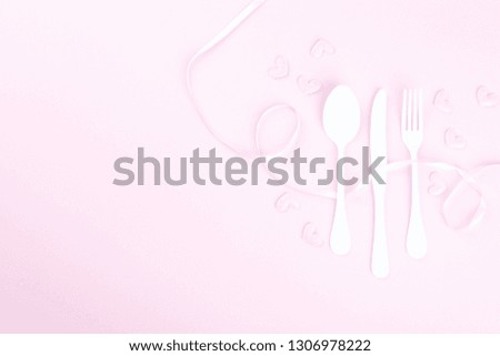 Festive table setting for Valentines Day with fork, knife and hearts  on pink pastel background.Set of silverware .Romantic dinner. Space for text. Top view  