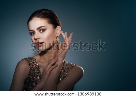 beautiful elegant woman in a golden dress with a make-up on her face and earrings on a dark background