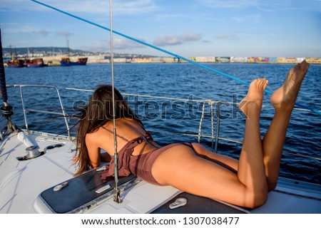 Young slim woman in a brown swimsuit enjoying her vacation on a yacht in the sea