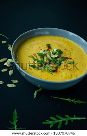 Pumpkin soup with cream and pumpkin seeds, served in a light bowl, top view. Proper and healthy food. Black background.
