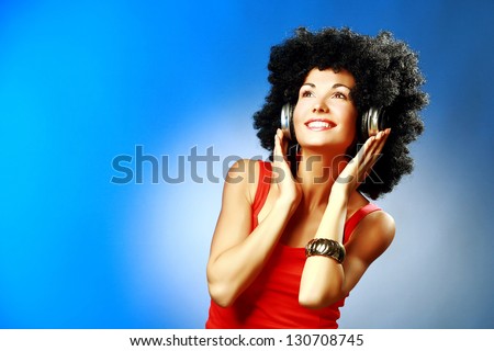 Beautiful smiling woman with afro hair listen to music with headphones on blue background