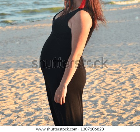 Pregnant woman posing for a photo shoot on vacation in a dark dress