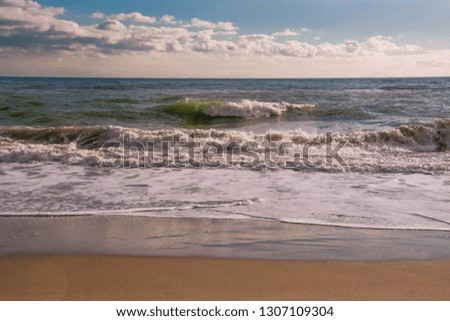 Autumn stormy sea on a sunny day with splashes from big waves. Large waves with white foam on the crest rise above the surface of the water and run to the shore. Background of beautiful nature