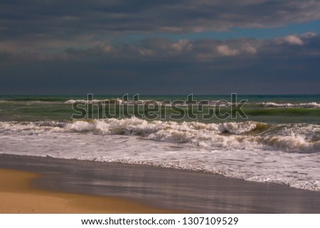Autumn stormy sea at sunset with splashes from big waves. Large waves with white foam on the crest rise above the surface of the water and run to the shore. Background of beautiful nature