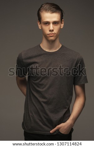 Picture of handsome Caucasian male model with stylish hair and brown eyes, dressed in casual grey t-shirt looking forward and standing indoors against studio brown background. Actor or student.