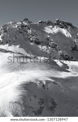 black and white picture of mountain landscape in Switzerland, Alps in winter. Ski trails are visible in a strong contrast between light and shadow