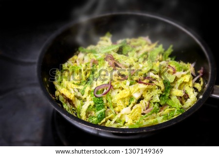 cooking green savoy cabbage with red onions in a black pan on a stove, healthy winter vegetable, selected focus, narrow depth of field Royalty-Free Stock Photo #1307149369