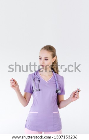 Woman doctor blonde young light gray background studio day beautiful one looks with a smile holding a marker pencil in her hand. Ready to record.