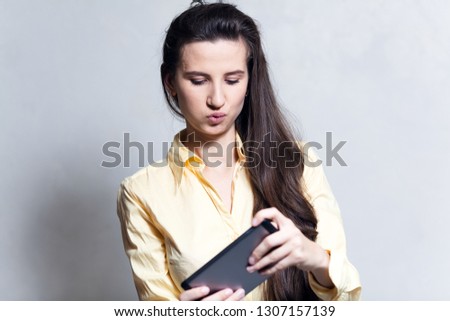 Portrait of young cheerful girl playing video games on smartphone over white background.