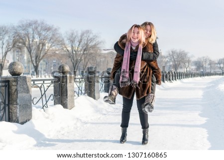 one woman carries another on her back along the fence on a snow-covered path in winter