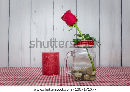 Romantic concept - Red candle, red rose in a jar with small rock