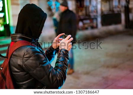 Man in a black hood shooting by mobile phone in the night street