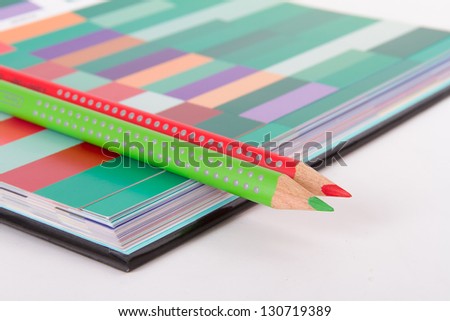 Red and green pencils on colorful art palette book, isolated on white background.