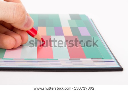 Hand holding red pencil on colorful art palette book, isolated on white background.