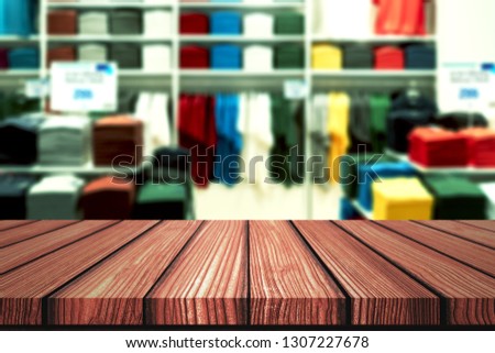 Wooden table with blurry background of casual boutique shop, shirt brand outlet or colorful clothes store for product display montage. Retail business of fashion product for online marketing backdrop.