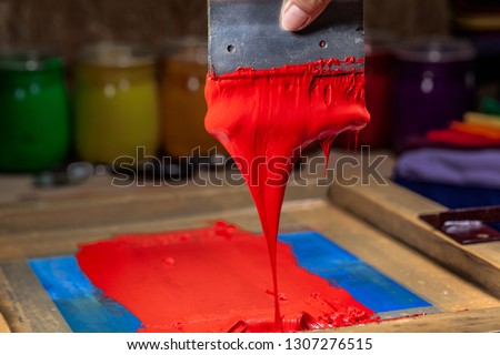 red color dripping from hand screen printing during printing tee shirt in tee shirt factory.