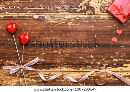 Couple of red hearts on sticks tied with a ribbon and gift box on a wooden background. Valentines day card concept.