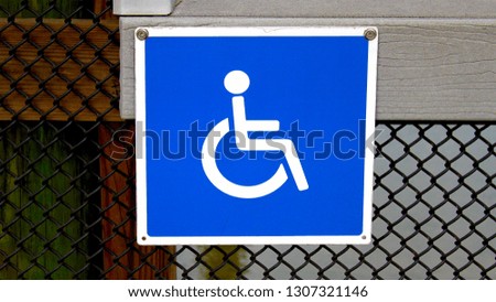 Handicap square metal sign in blue and white. Handicap metal sign attached to a metal fence at the entrance of a park.