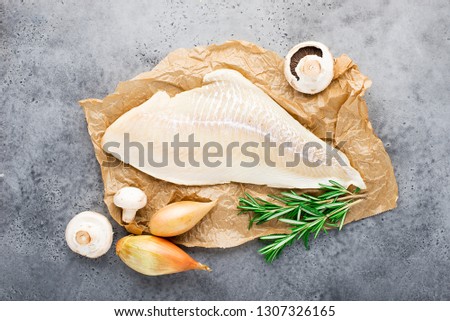Wild northern white cod fillet fillet on parchment with shallot onions, olive oil, thyme, rosemary, champignons for cooking healthy meals for the whole family. Top view