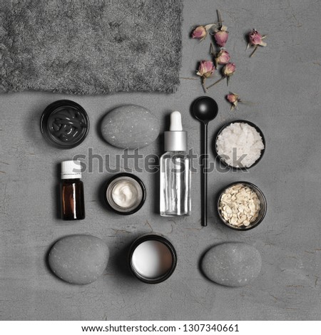 Composition of natural organic cosmetics, pebble, terry towel and dry roses on grey background. Top view point, flat lay.