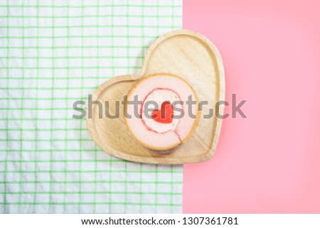 Strawberry cake in a heart shape wooden plate on green tablecloth and pink background. Top view, close up. Love concept with copy space.