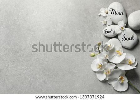 Flat lay composition of orchid flowers and zen stones with words Mind, Body, Soul on light background. Space for text 
