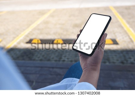Mockup image of a hand holding black mobile phone with blank white desktop screen on the street