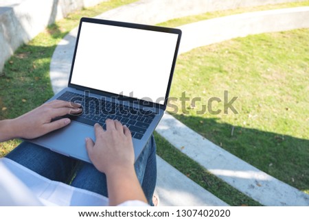 Mockup image of a woman using and typing on laptop with blank white screen , sitting in the outdoors with nature background