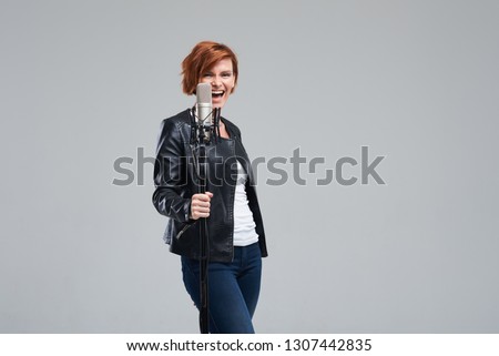 Portrait of rock singer wearing leather jacket and keeping static mic, sings a song loudly on grey background. Concept of rock music and rave