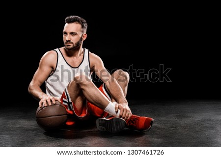 serious basketball player sitting with ball on black background