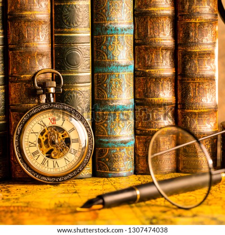 Antique clock on the background of vintage books. Mechanical clockwork on a chain. Fountain pen and glasses.
