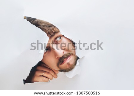 Portrait of a man looking through the hole in white paper. Distrustful look. Man's curiosity and gossip. A jealous husband. Royalty-Free Stock Photo #1307500516