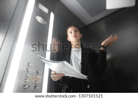 Background with a young female office worker throwing papers in the lift. Background with a businesswoman in the elevator throwing documents up. Blurry photo background.
