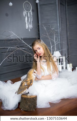 Cute girl with blond hair in a white dress with a white owl on her arms
