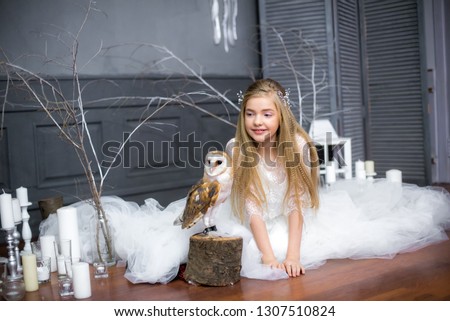 Cute girl with blond hair in a white dress with a white owl on her arms
