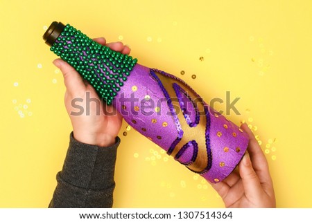 Diy Mardi Gras bottle purple self adhesive paper, green bead, carnival mask, sequins yellow background. Gift idea, decor Mardi Gras, Fat, Shrove Tuesday. Step by step. Top view. Process children craft