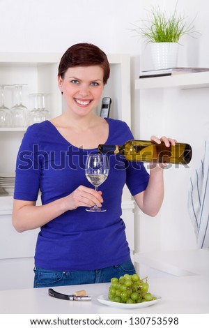 young woman pouring white wine in a glass in her modern kitchen