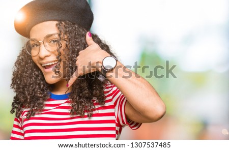 Young beautiful woman with curly hair wearing glasses and fashion beret smiling doing phone gesture with hand and fingers like talking on the telephone. Communicating concepts.