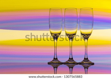 A row of three empty champagne glasses with a multicolored rainbow of light painting behind them