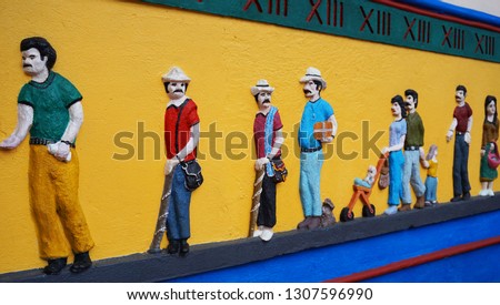 Stucco design on the yellow wall - different people in colorful clothes with a sign of the 18th century. Hand made street art, Guatape, Kolombia
