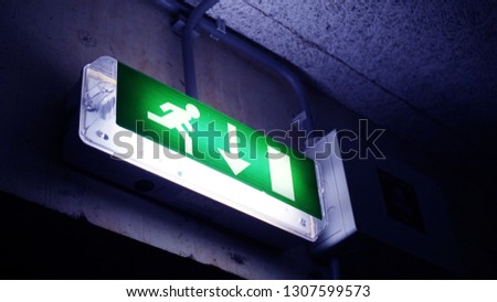 Glowing on a green background sign Exit with a down arrow, a running man in a brick building by the door in dark colors